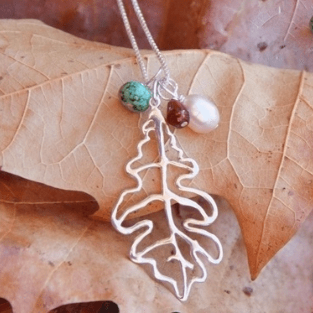 Oak leaf shaped silver necklace with three gems resting on autumn leaves-Winchester Creek Farms